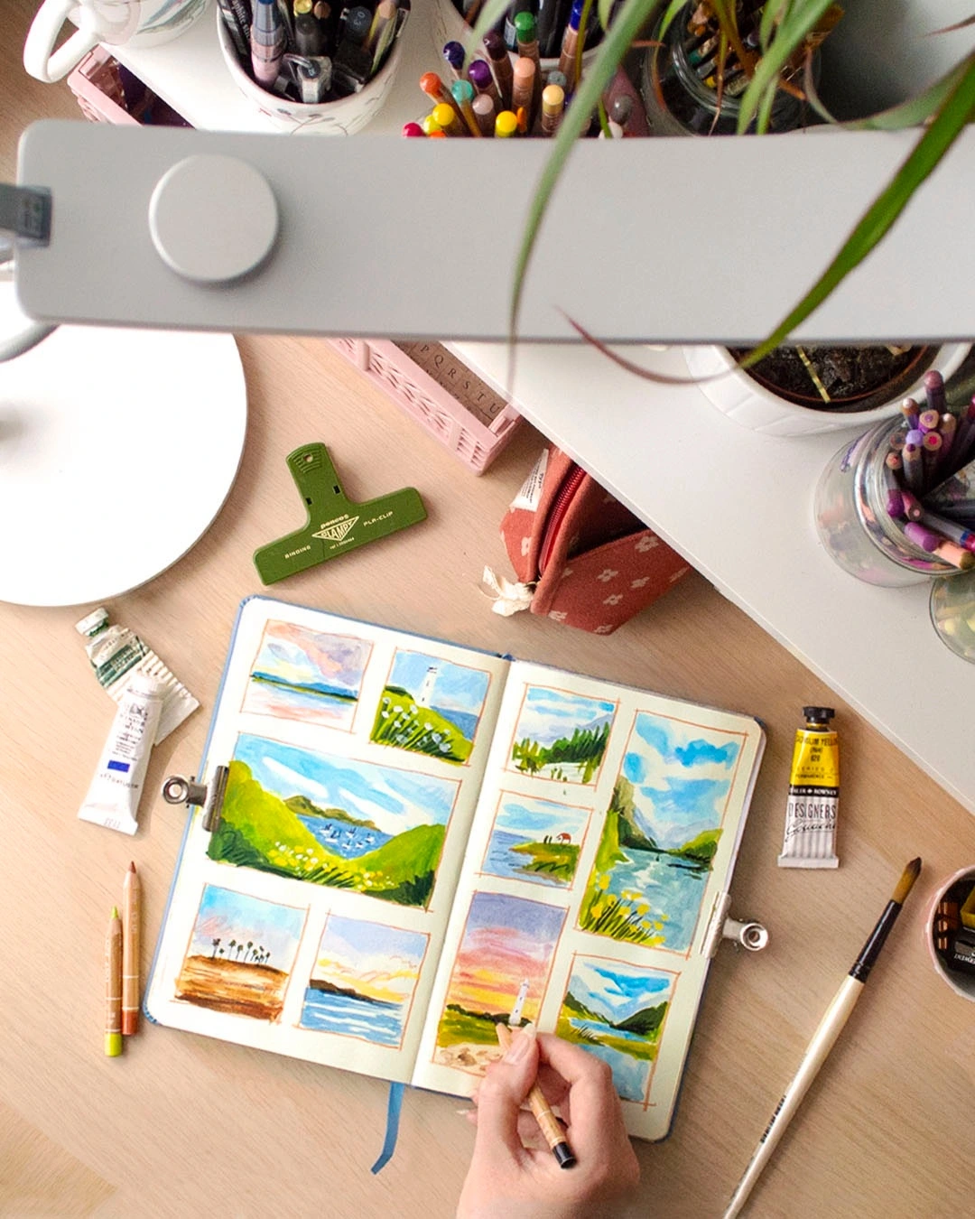 Artist painting in a sketchbook beneath a BenQ desk lamp